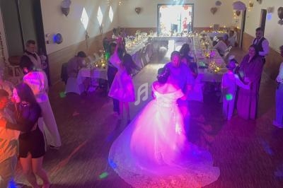 Des invités dansent dans une salle de réception décorée, éclairée par des lumières colorées, lors d'un mariage.