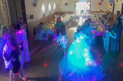 Des invités dansent dans une salle décorée pour un mariage, éclairée par des lumières colorées et des guirlandes lumineuses.