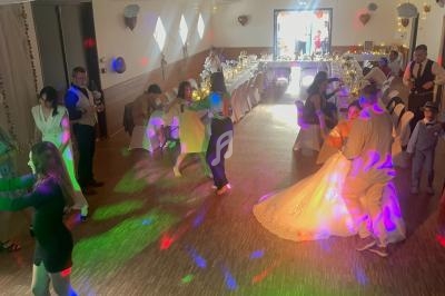 Des invités dansent dans une salle de réception décorée, éclairée par des lumières colorées, avec une table festive au fond.