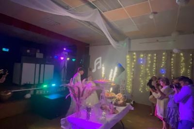 Un couple de mariés devant une table décorée avec des gâteaux illuminés par des cierges, entourés d'invités.