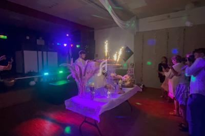 Une salle de fête sombre avec une table décorée, un gâteau illuminé par des cierges et des invités rassemblés.