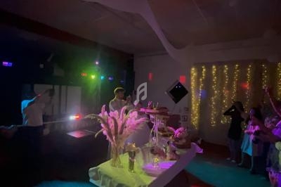 Salle décorée pour une fête avec éclairage coloré, table garnie et invités rassemblés près d'un mur illuminé.