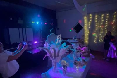 Salle de réception décorée avec guirlandes lumineuses, table garnie de fleurs et desserts, éclairage tamisé et coloré.