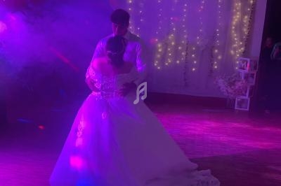 Un couple danse dans une salle décorée de guirlandes lumineuses, éclairée par des lumières colorées et de la fumée.
