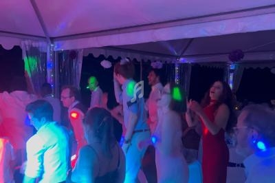 Des personnes dansent et s'amusent sous une tente éclairée par des lumières colorées lors d'une fête nocturne.