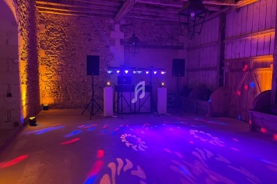 Salle en pierre éclairée par des lumières colorées, avec une installation de DJ et des projecteurs.