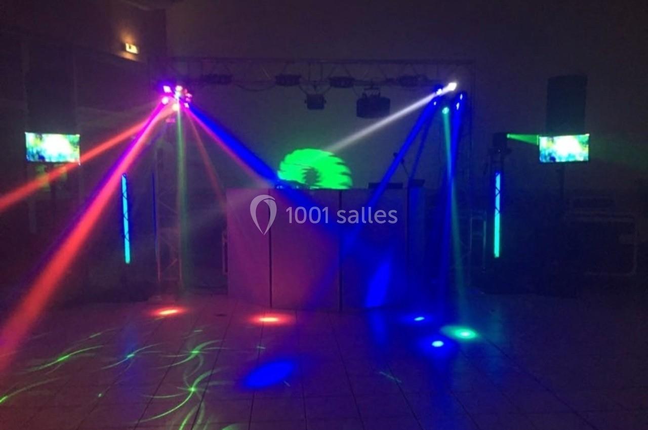 Jeu de lumières colorées projetées dans une salle sombre avec un équipement de sonorisation en arrière-plan.