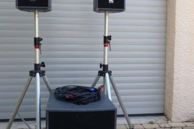 Deux enceintes sur trépieds et un caisson de basses posés sur un sol pavé devant une porte de garage.