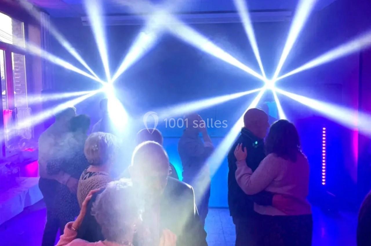 Des couples dansent sous des jeux de lumière colorés dans une salle sombre, créant une ambiance festive.