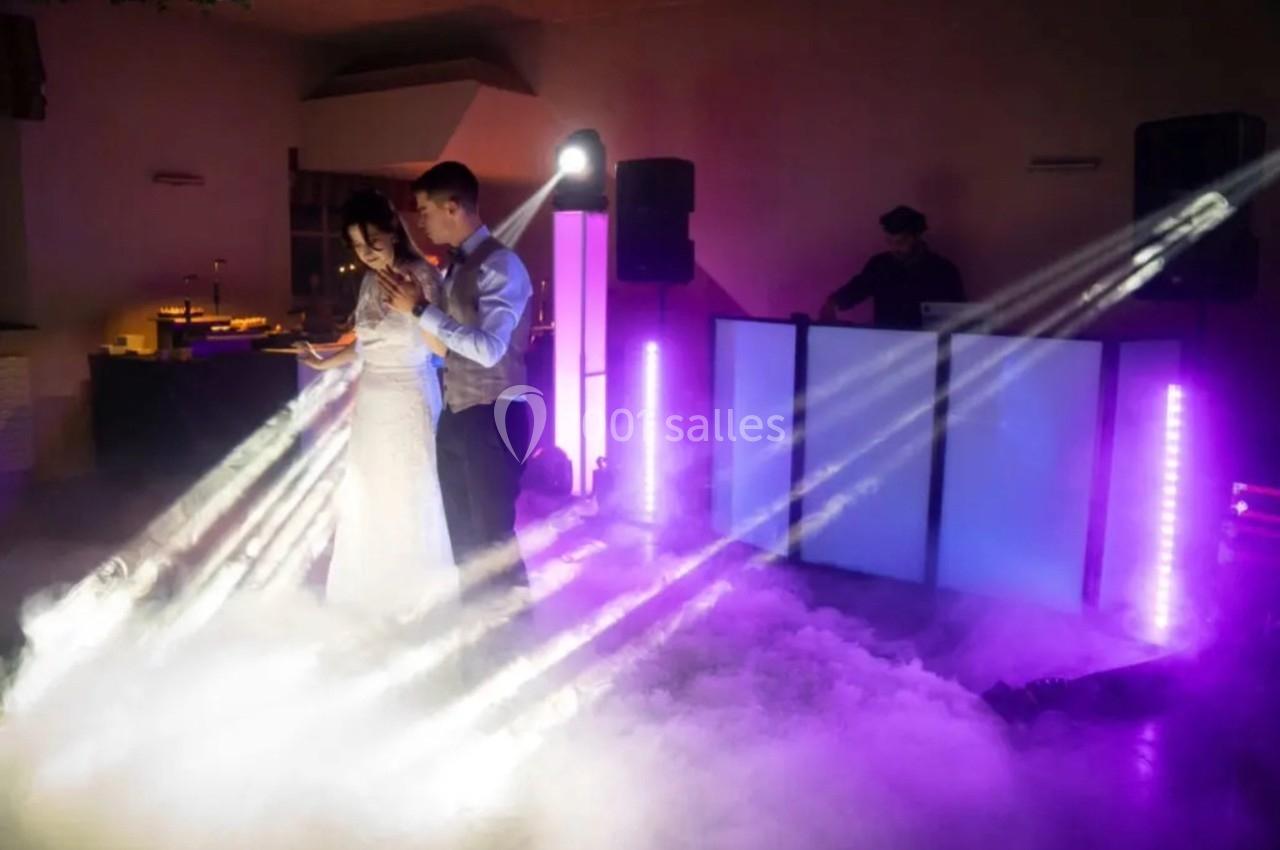 Un couple danse dans une ambiance festive avec éclairages colorés et fumée, un DJ en arrière-plan.