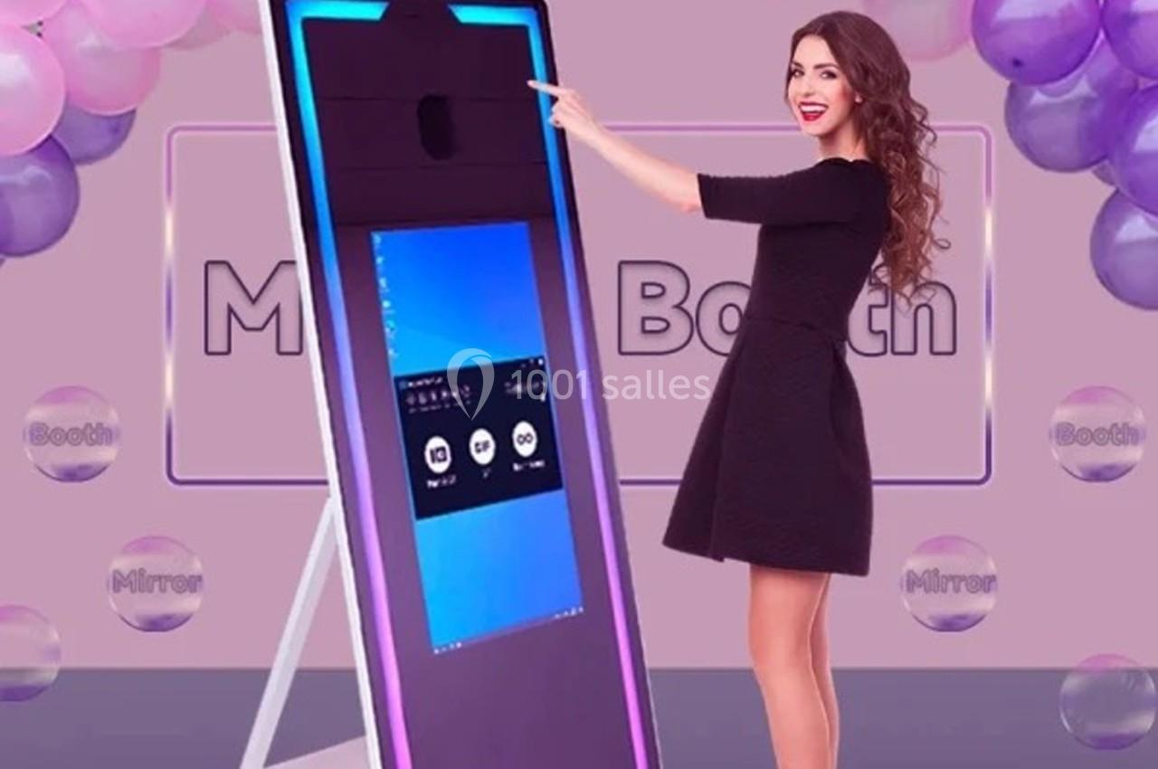 Femme interagissant avec un miroir photo interactif entouré de ballons dans un décor festif.