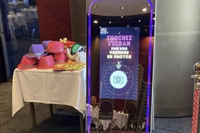 Deux femmes souriantes se tiennent près d'une borne photo dans un espace intérieur avec des tables et des chaises en arrière…