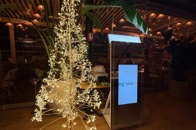 Deux femmes souriantes se tiennent près d'une borne photo dans un espace intérieur avec des tables et des chaises en arrière…