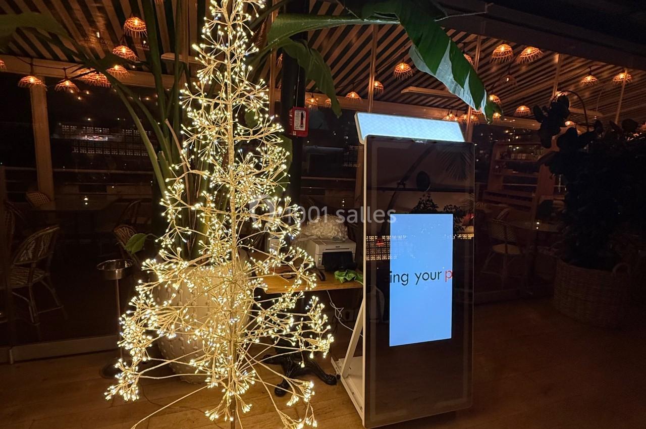 Un arbre décoratif illuminé à côté d'une borne interactive dans un espace intérieur avec un éclairage tamisé.