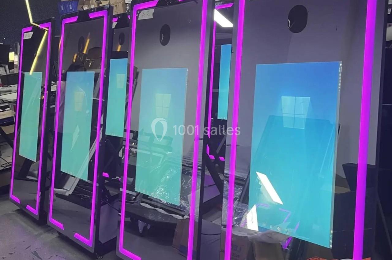 Écrans verticaux avec cadres lumineux roses alignés dans un atelier, reflétant partiellement l'environnement.