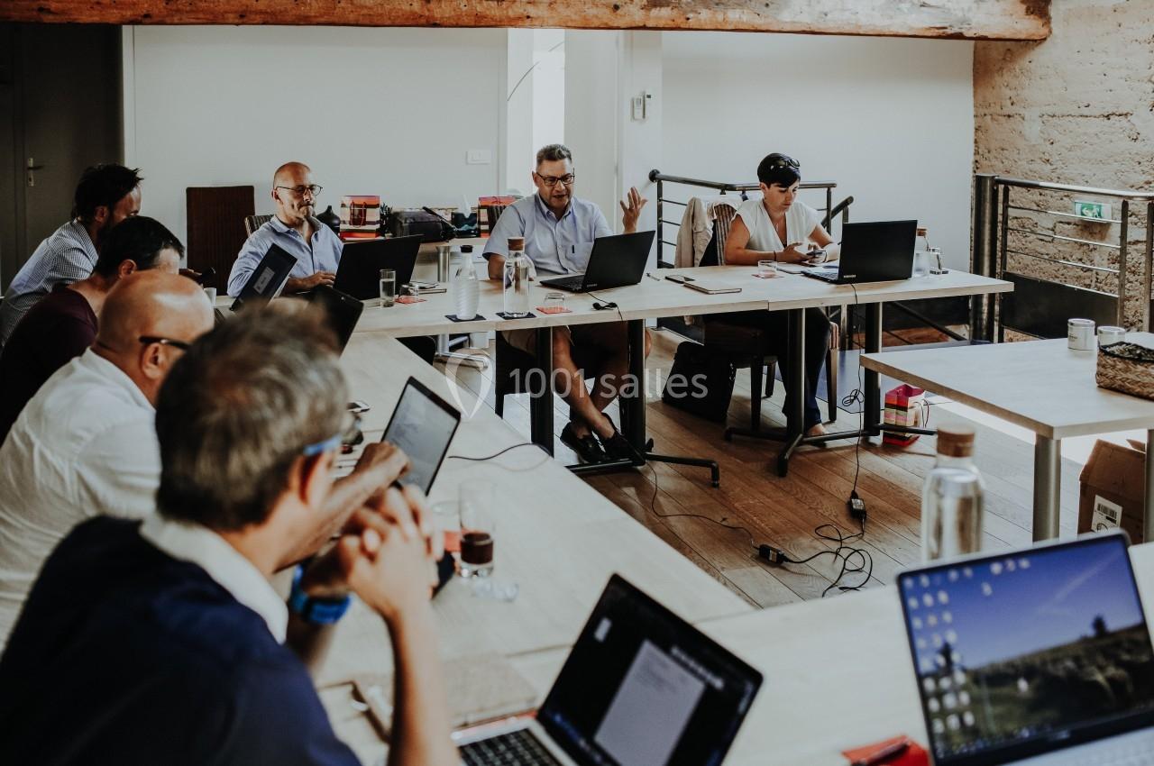 Des personnes participent à une réunion autour de tables en bois, avec des ordinateurs portables et des documents.