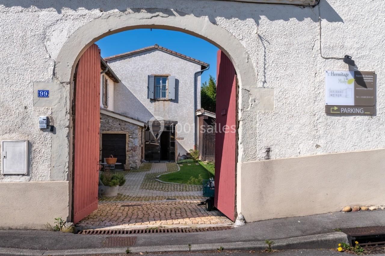 Entrée d'une cour pavée avec un bâtiment en pierre et un panneau indiquant un parking sur le mur.