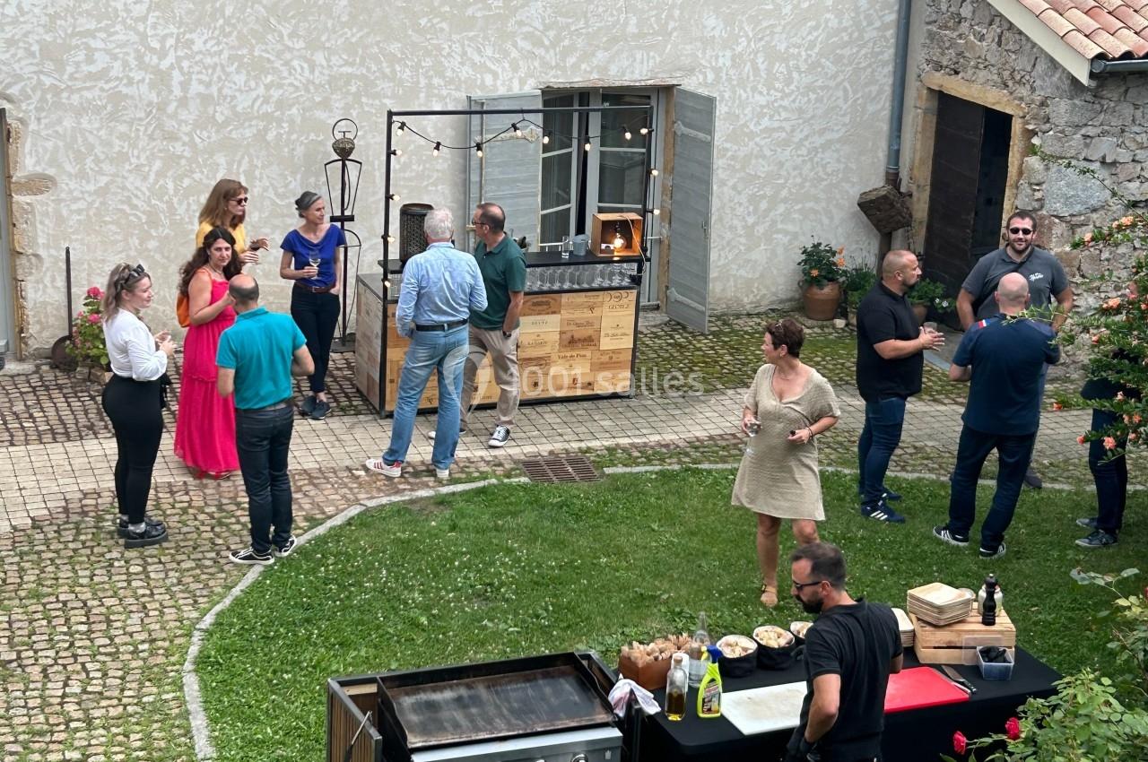 Personnes rassemblées dans une cour pavée avec un barbecue et une table de buffet en premier plan.