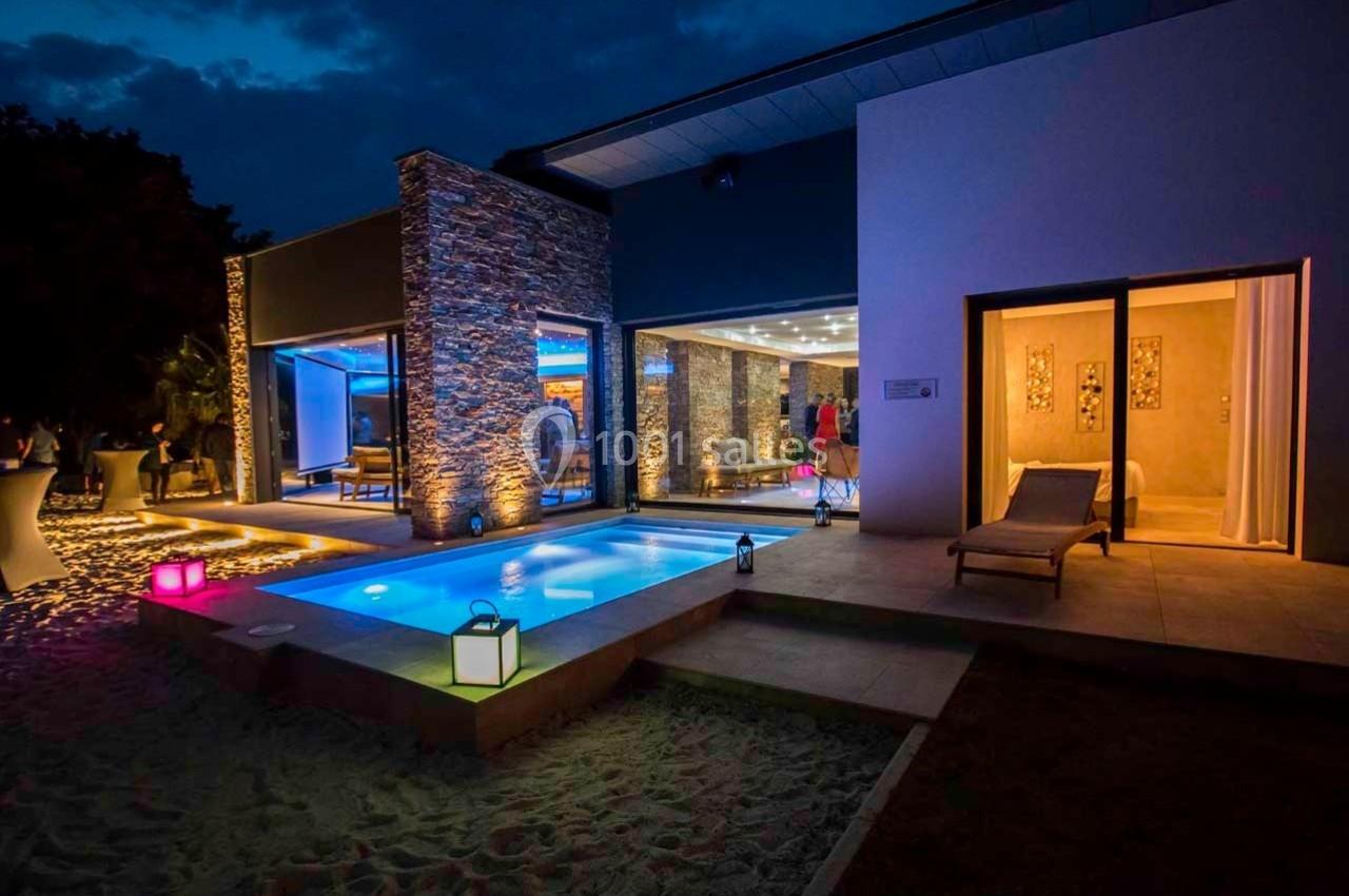 Maison moderne avec piscine éclairée la nuit, entourée de lanternes colorées et d'une terrasse aménagée.