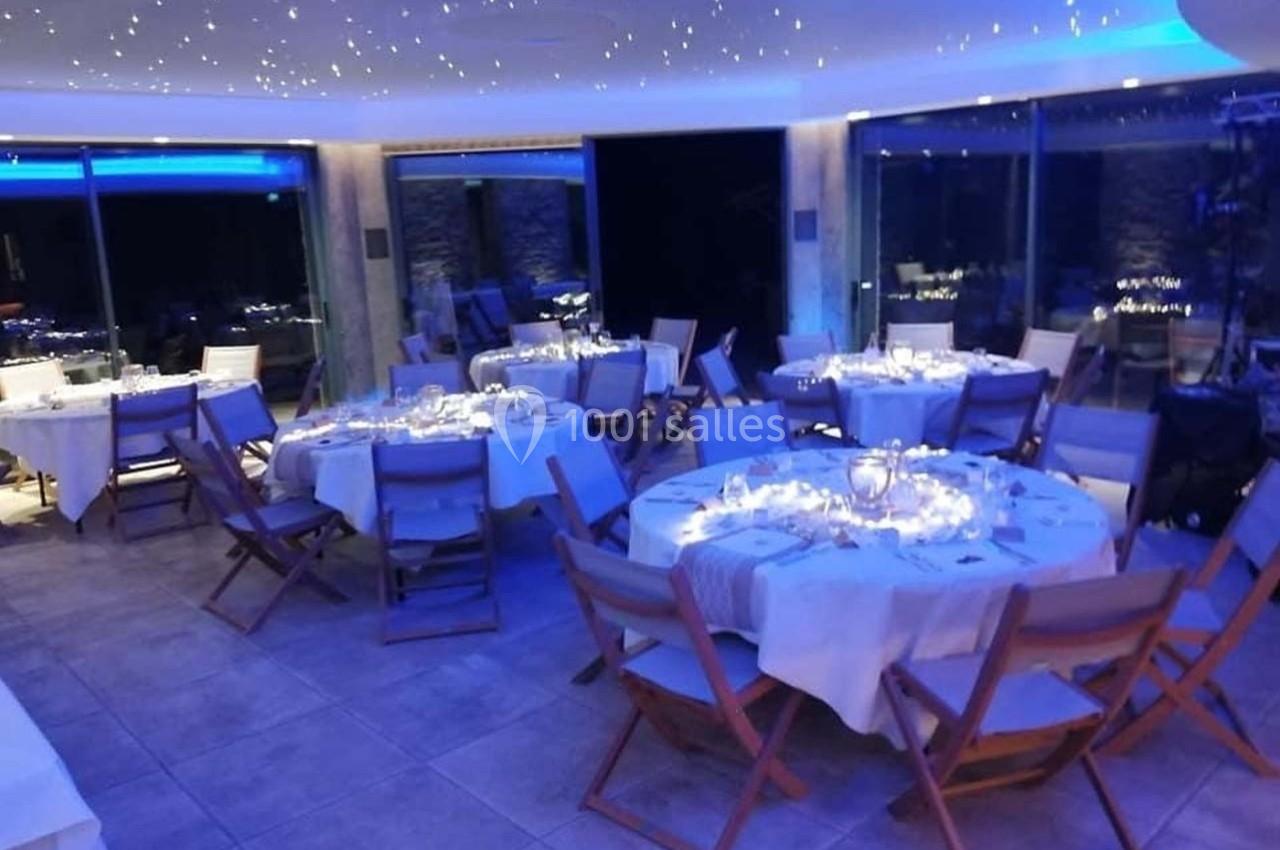 Salle de réception élégante avec tables rondes dressées, éclairage tamisé et ambiance lumineuse bleutée.