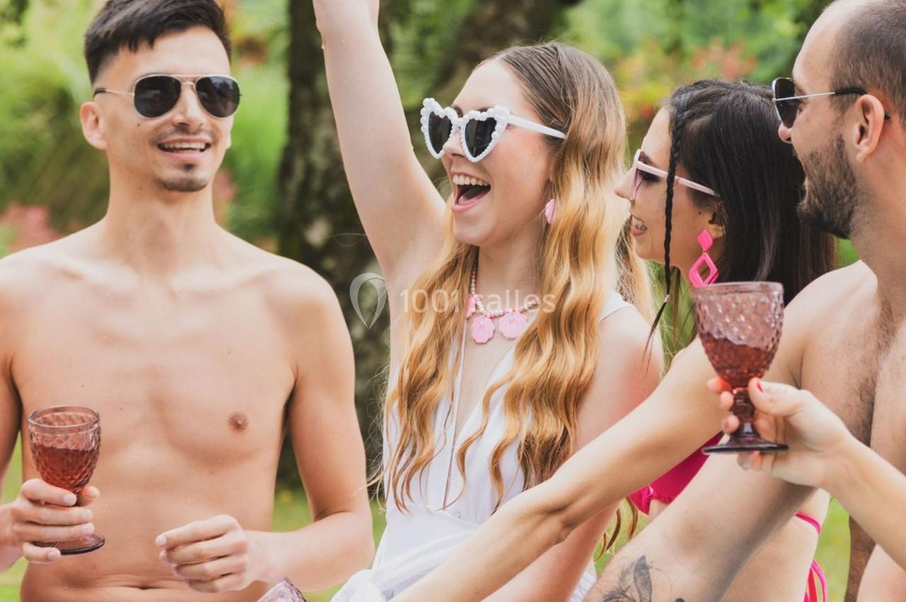 Quatre personnes souriantes discutent et trinquent avec des verres colorés dans un cadre extérieur verdoyant.
