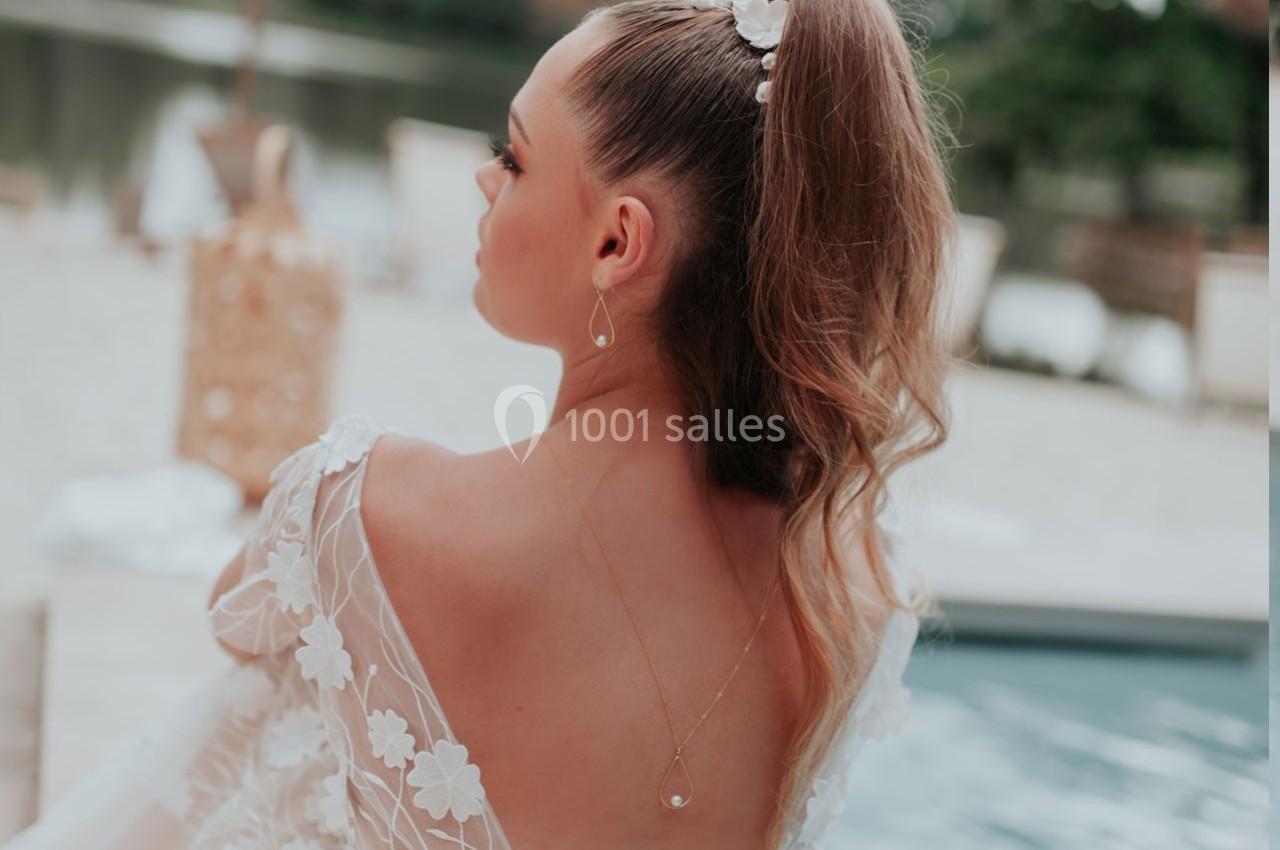 Femme de dos avec une coiffure en queue de cheval ornée, portant une robe à motifs floraux près d'une piscine.