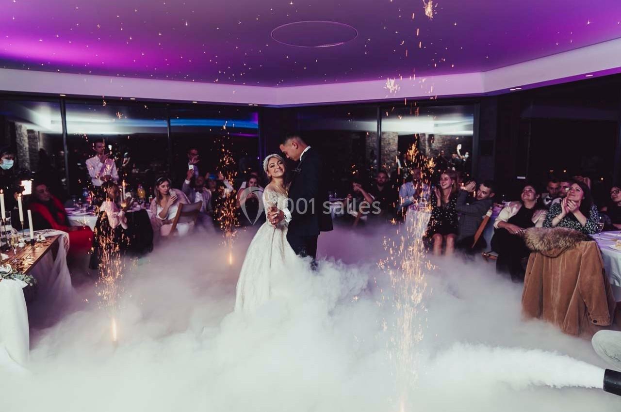 Un couple danse au centre d'une salle décorée, entouré de fumée et d'étincelles, sous le regard des invités.