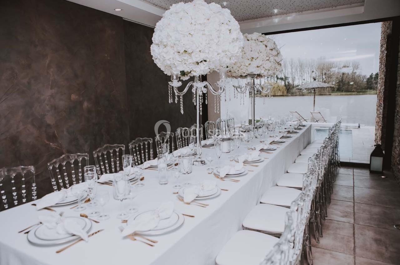 Table élégamment dressée avec nappes blanches, vaisselle raffinée et centres de table ornés de fleurs blanches.