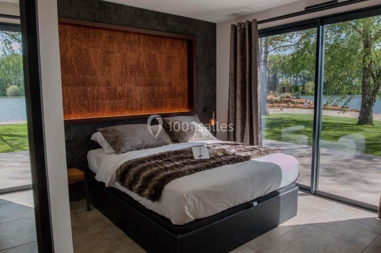 Chambre avec lit double, grande baie vitrée donnant sur un jardin verdoyant et un plan d'eau.