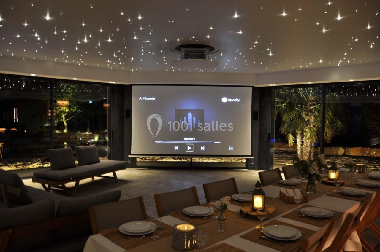 Salle moderne avec un plafond étoilé, un écran de projection affichant Spotify, et une table dressée pour un repas.