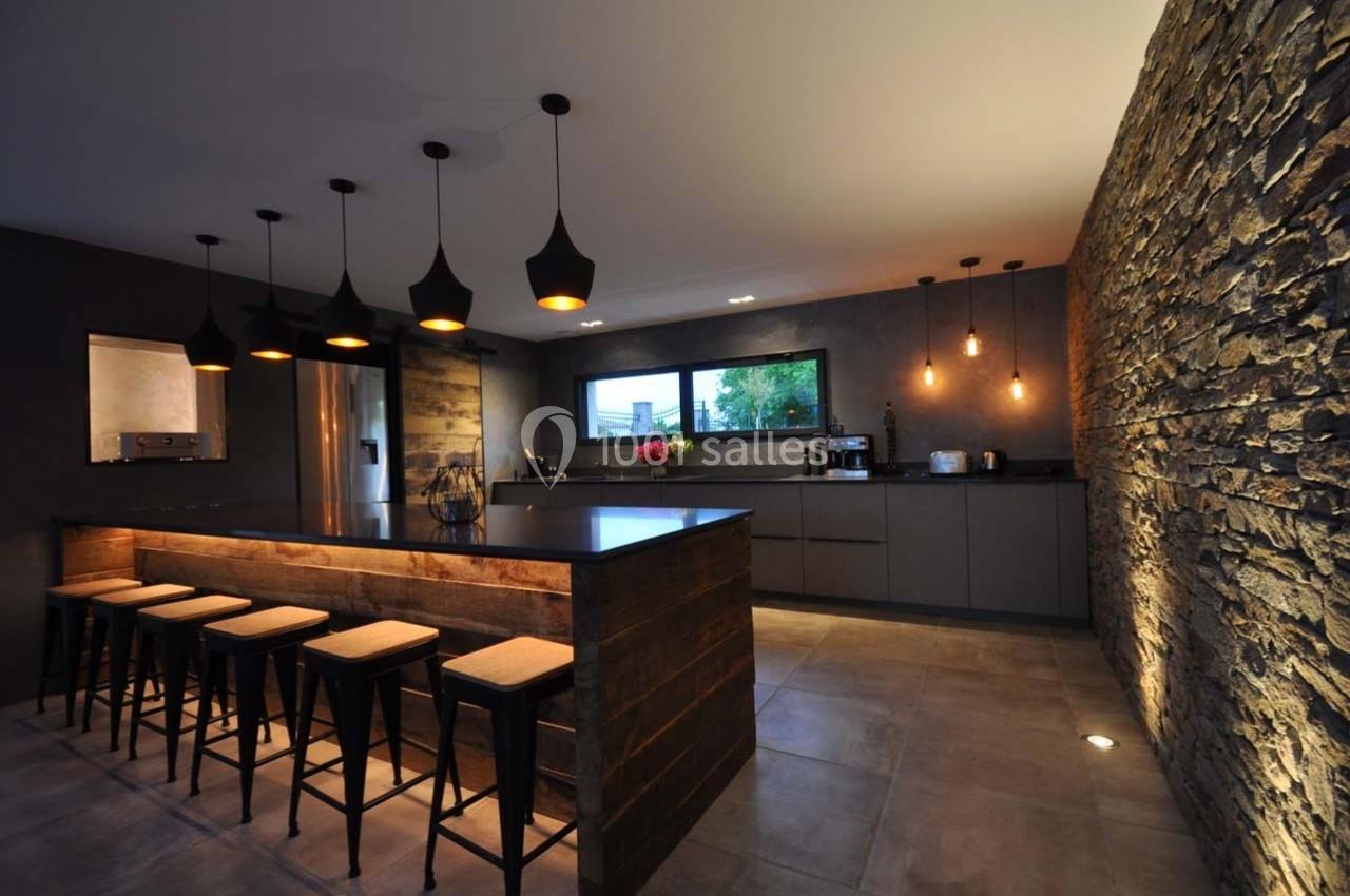 Cuisine moderne avec îlot central en bois, tabourets, éclairage suspendu et mur en pierre apparente.