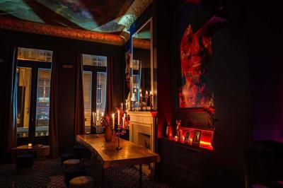 Salle sombre avec éclairage tamisé rouge, mobilier élégant, chandeliers et étagères illuminées derrière un bar.