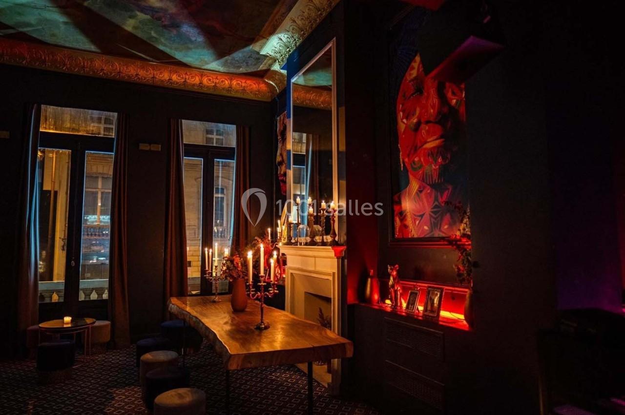 Salle sombre et élégante avec une grande table en bois, chandeliers allumés, miroirs et décoration artistique colorée.
