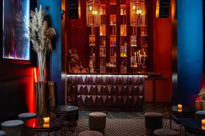 Salle sombre avec éclairage tamisé rouge, mobilier élégant, chandeliers et étagères illuminées derrière un bar.