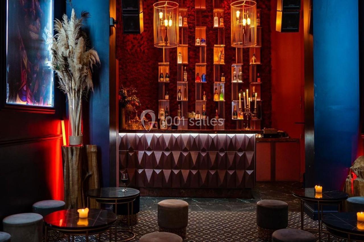 Bar élégant avec comptoir géométrique, étagères illuminées de bouteilles, tabourets bas et ambiance tamisée.