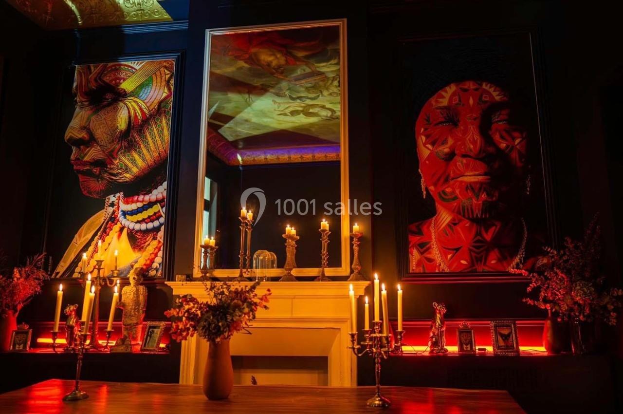 Salle sombre décorée avec des portraits colorés, des chandeliers allumés et une cheminée ornée de bougies.