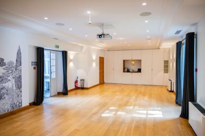 Salle de réunion lumineuse avec tables disposées en U, chaises jaunes, écran de projection et tableau blanc.