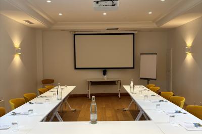 Salle de réunion lumineuse avec tables disposées en U, chaises jaunes, écran de projection et tableau blanc.