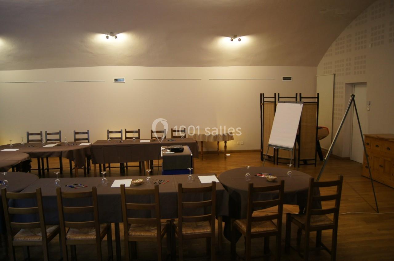 Salle de réunion avec tables disposées en U, chaises en bois, tableau de conférence et éclairage tamisé.