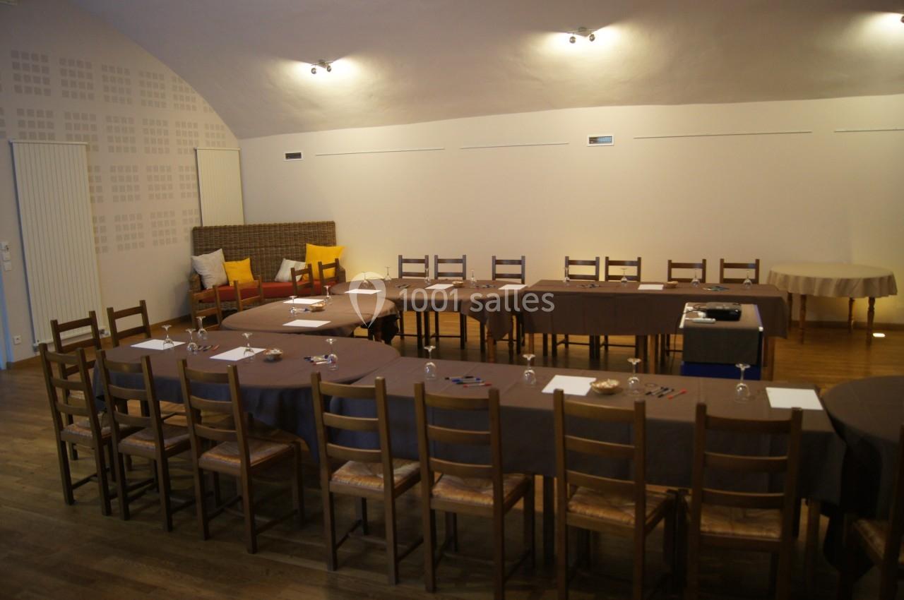 Salle de réunion avec tables disposées en U, chaises en bois, feuilles, stylos et éclairage tamisé.