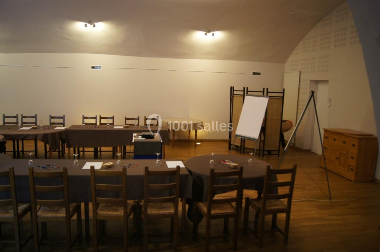 Salle de réunion avec tables disposées en U, chaises en bois, paperboard et éclairage tamisé.