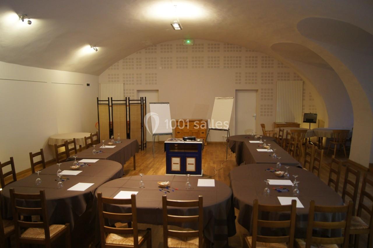 Salle de réunion avec tables en U, chaises en bois, paperboards, et matériel de prise de notes sur les tables.