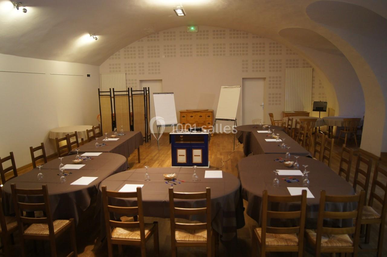 Salle de réunion avec tables disposées en U, chaises en bois, tableaux blancs et éclairage tamisé.