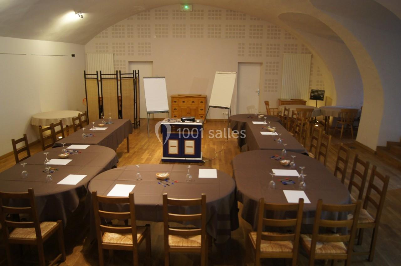 Salle de réunion avec tables disposées en U, chaises en bois, paperboards, et matériel de présentation au centre.