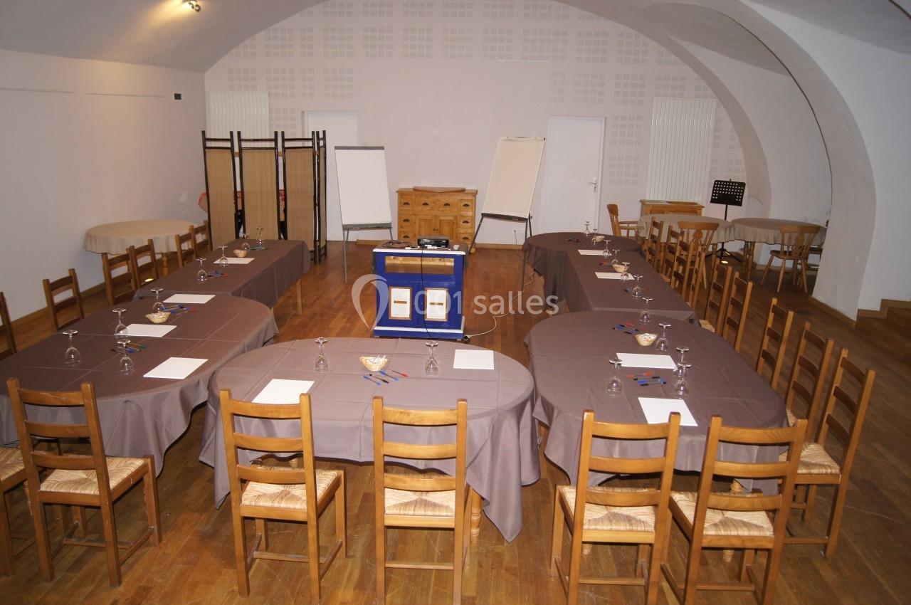 Salle de réunion aménagée en U avec tables, chaises en bois, paperboards et matériel de présentation.