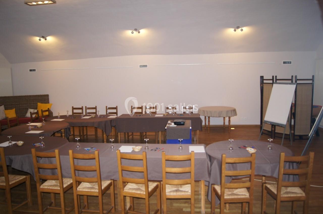 Salle de réunion avec tables disposées en U, chaises en bois, tableau de conférence et éclairage au plafond.