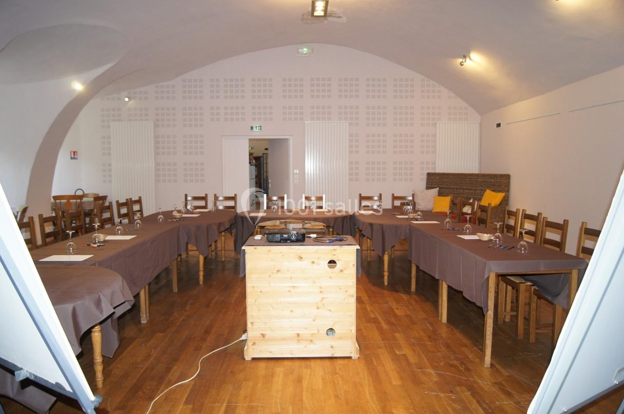 Salle de réunion avec tables en U, nappes brunes, chaises en bois et projecteur sur une table centrale.