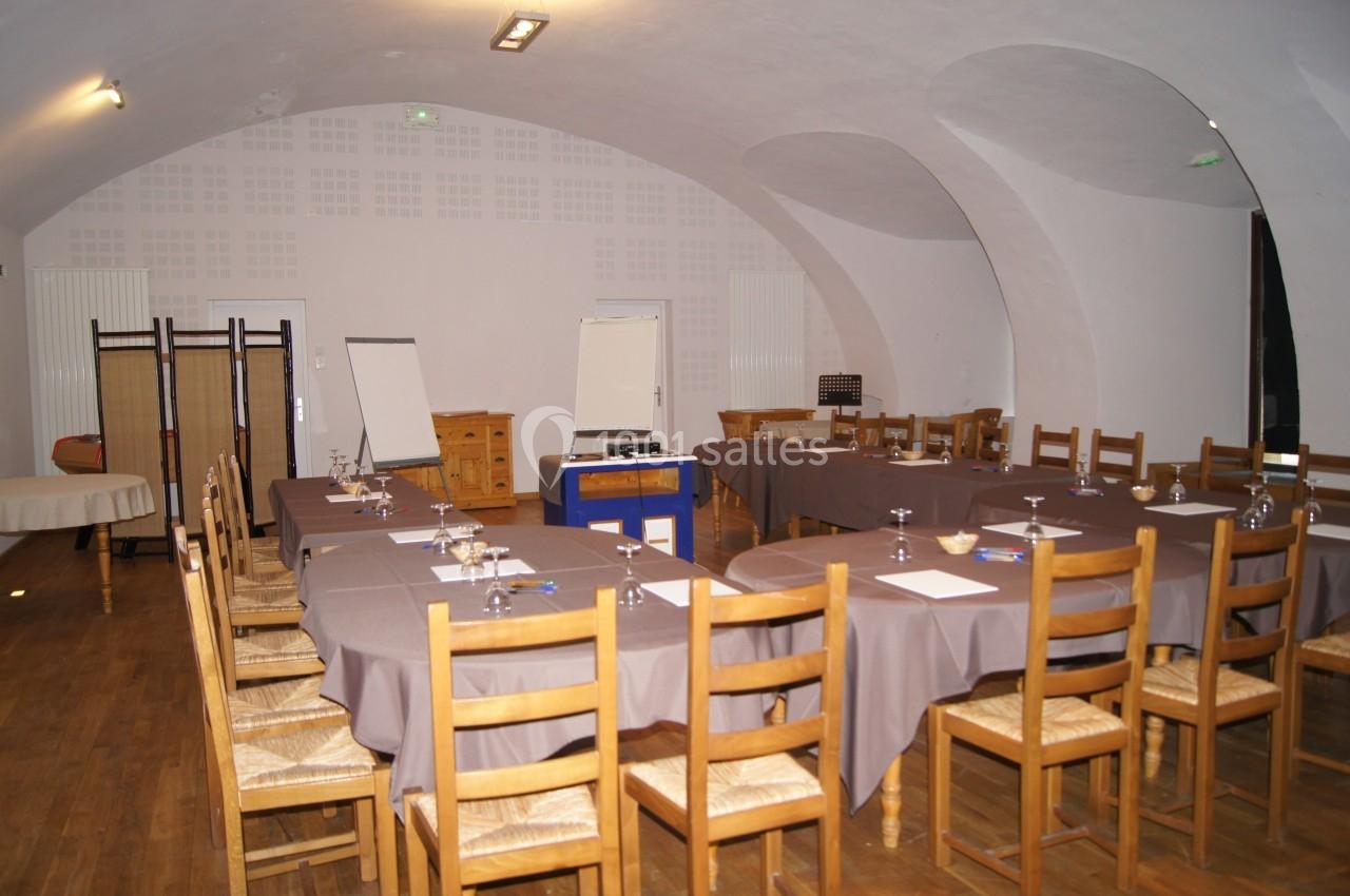 Salle de réunion voûtée avec tables disposées en U, chaises en bois, paperboard et matériel de présentation.