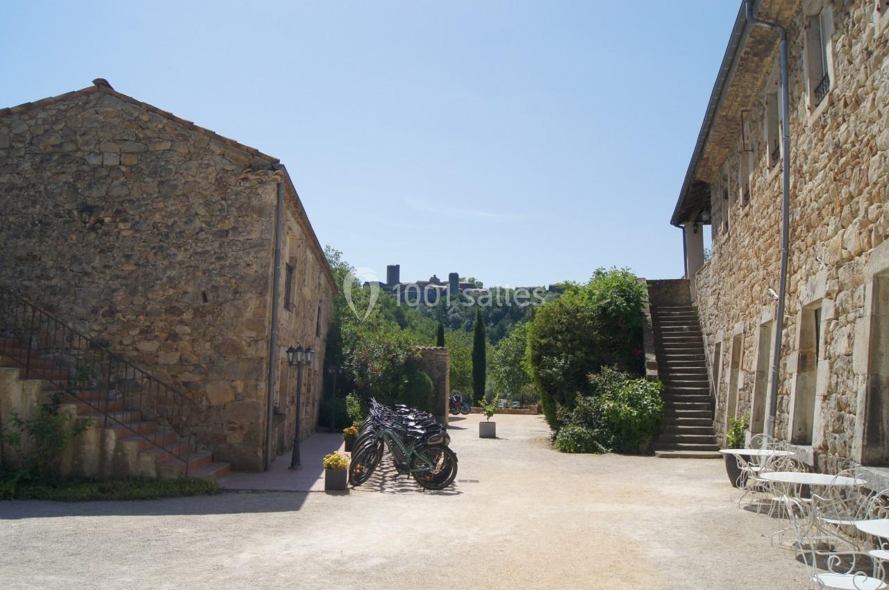 Cour ensoleillée avec bâtiments en pierre, vélos stationnés au centre et vue sur un château au loin.