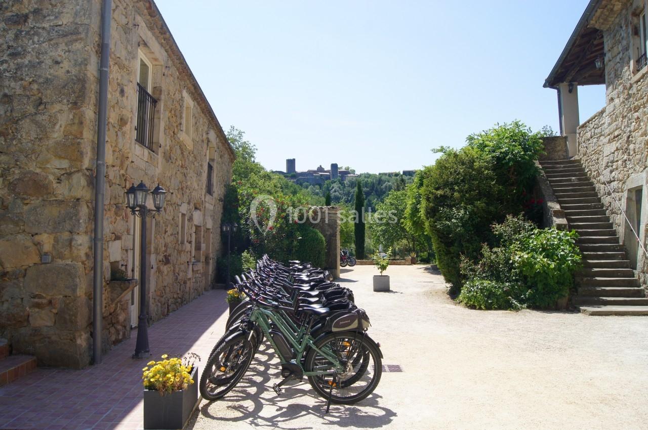 Alignement de vélos devant des bâtiments en pierre dans une ruelle ensoleillée avec vue sur un château au loin.